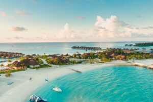 Une vue aérienne époustouflante d'une plage tropicale des Maldives avec des eaux turquoise claires et des complexes hôteliers le long du rivage.