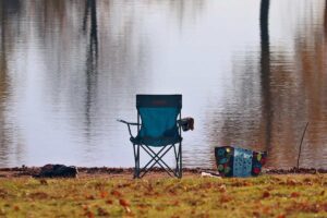 Une chaise pliante bleue et un sac reposent près d'un lac calme