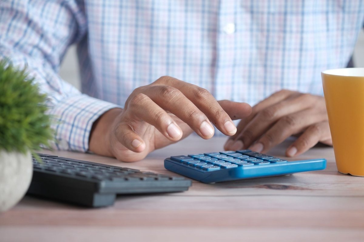 Personnes mains au clavier et à la calculatrice sur un bureau avec tasse et plante
