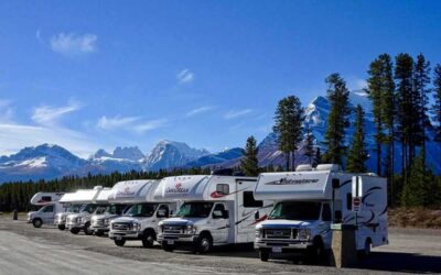 Rangée de camping-cars garés côte à côte, chaîne montagneuse enneigée en arrière-plan
