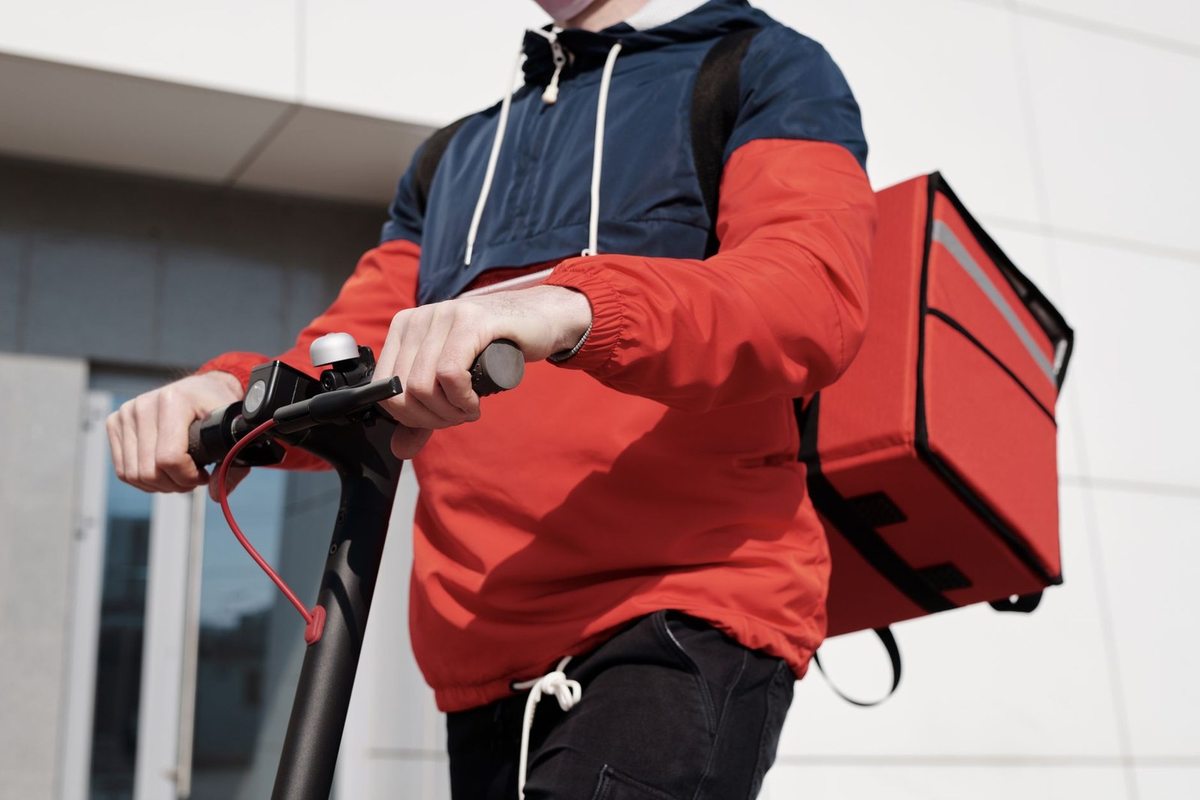 Individu sur trottinette avec sac rouge devant un édifice contemporain