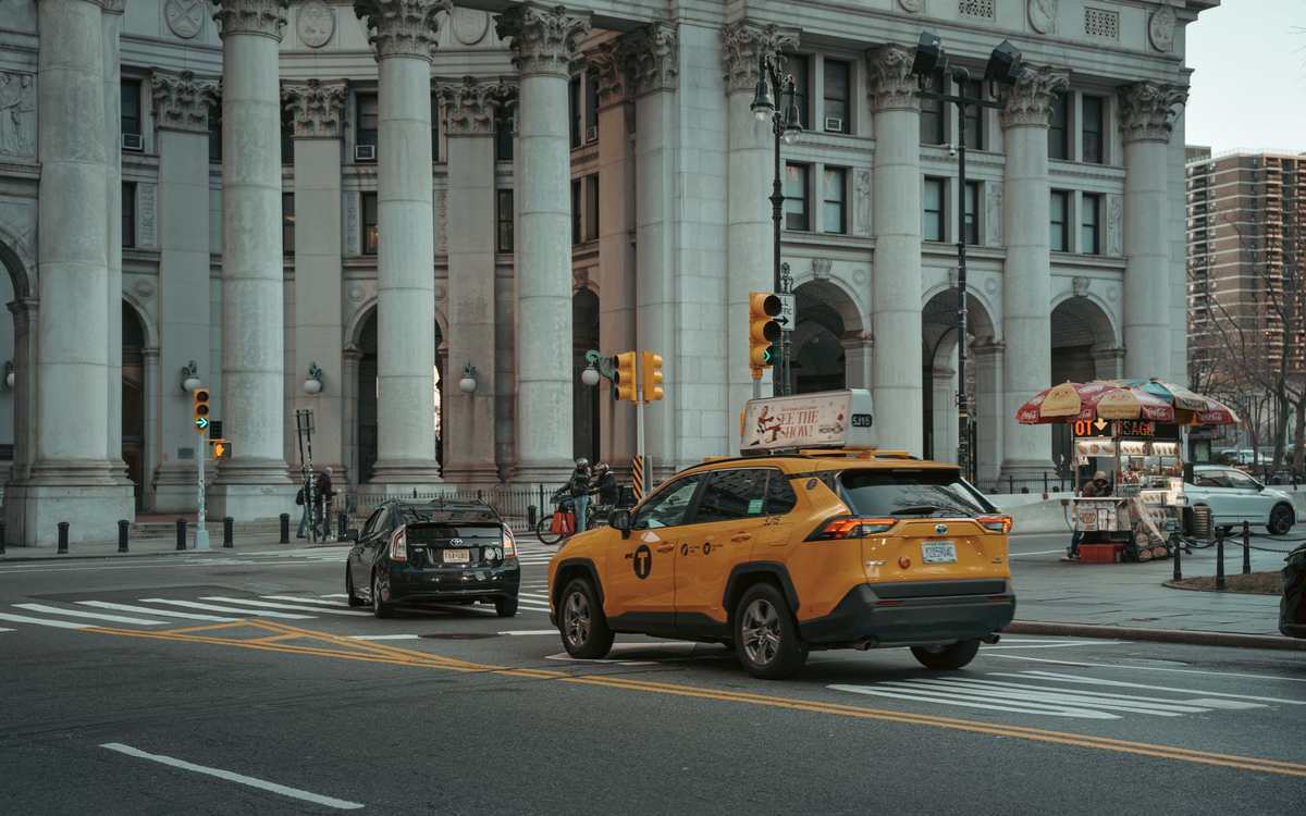 Taxi jaune et voiture noire devant un édifice monumental avec colonnes Taxi jaune et voiture noire devant un édifice monumental avec colonnes
