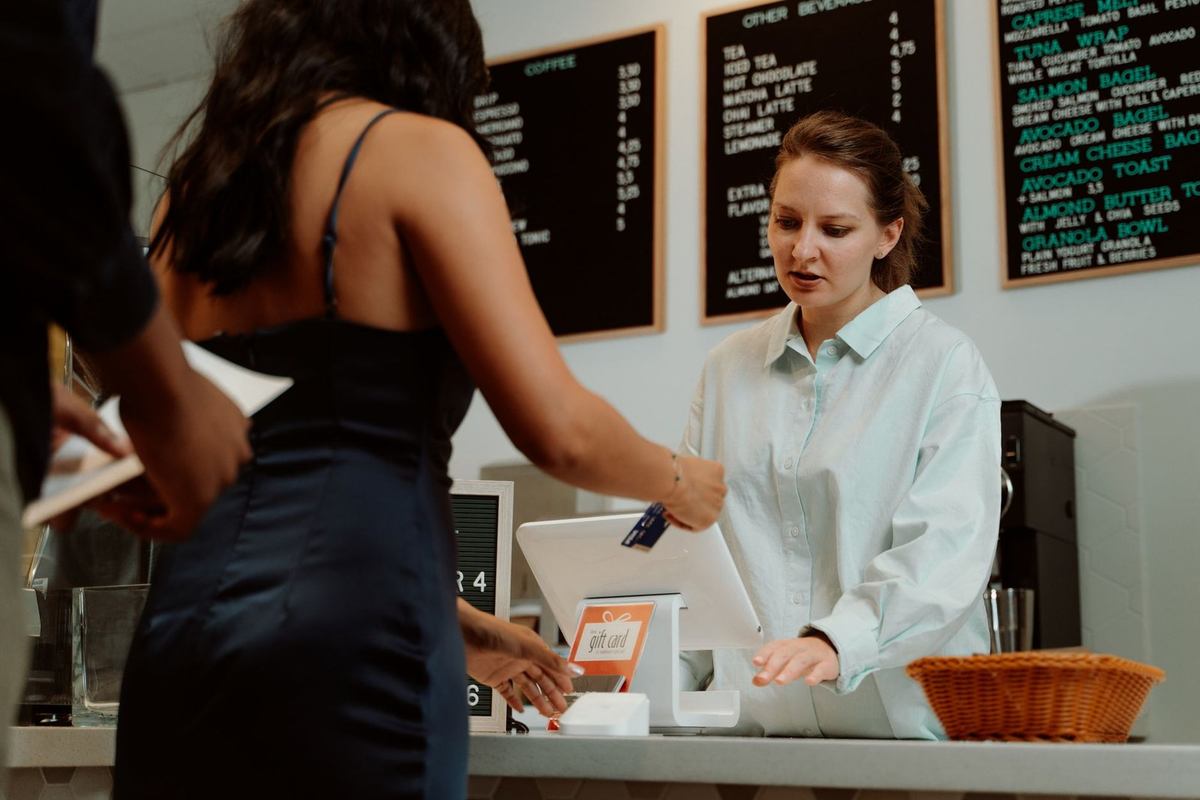 Femme payant à un guichet, serveuse en blanc, menu sur le mur, caisse, panier