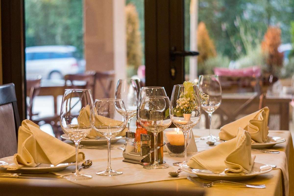 Table mise en place avec des ustensiles et des verres, devant des fenêtres donnant sur un jardin Table mise en place avec des ustensiles et des verres, devant des fenêtres donnant sur un jardin