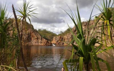 Enfants baignant dans un lac encadré de falaises rocheuses boisées sous ciel nuageux