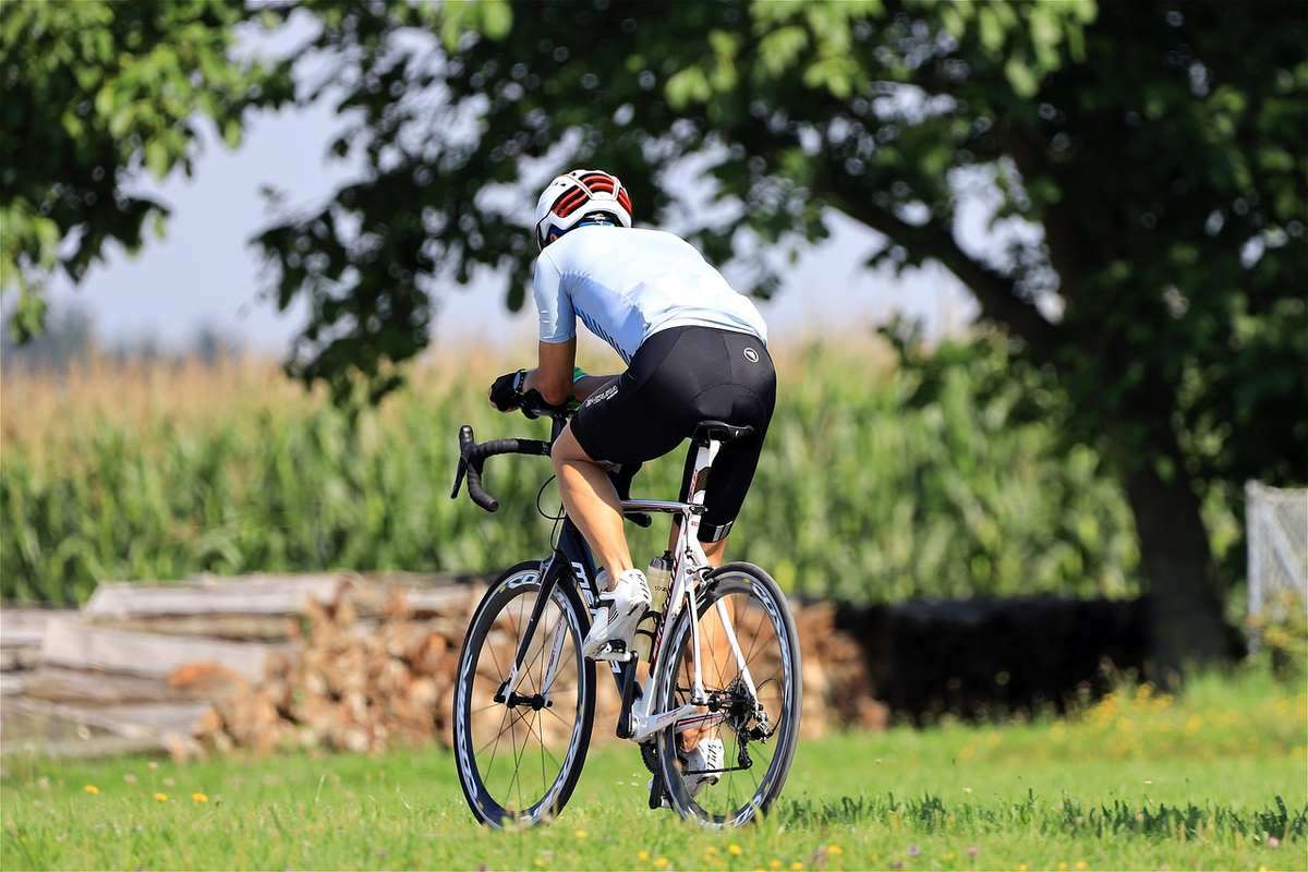 Cycliste en jersey blanc et short noir pédalant sur une route campagnarde avec champs et arbres