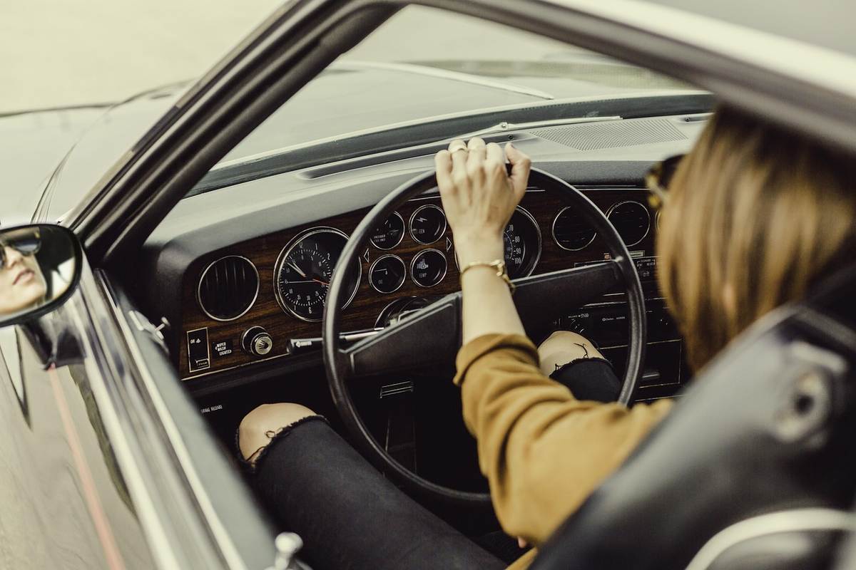Une femme conduit une voiture, main sur le volant, regard vers l'avant
