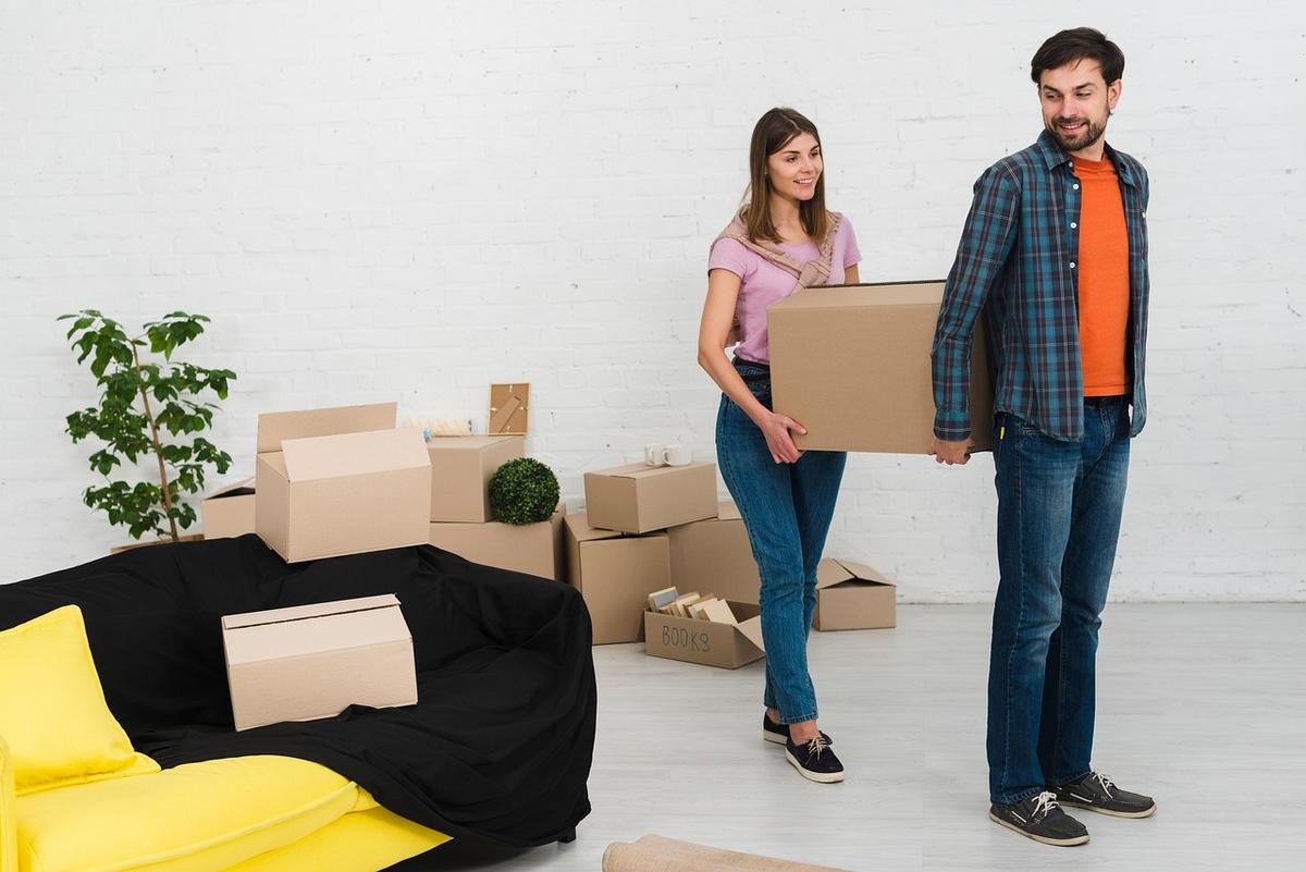 Deux personnes portent des cartons dans une salle vide Deux personnes portent des cartons dans une salle vide