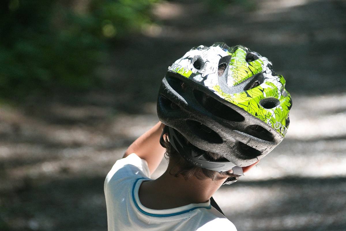 Un enfant ajuste son casque de vélo sur un chemin ombragé Un enfant ajuste son casque de vélo sur un chemin ombragé