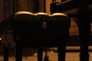 Un tabouret de piano noir avec logo lyre éclairé dans une pièce sombre
