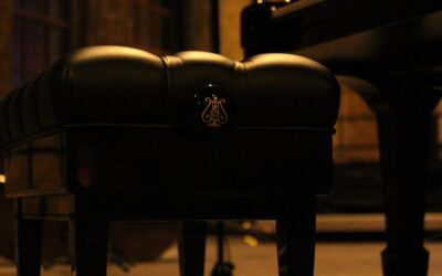 Un tabouret de piano noir avec logo lyre éclairé dans une pièce sombre