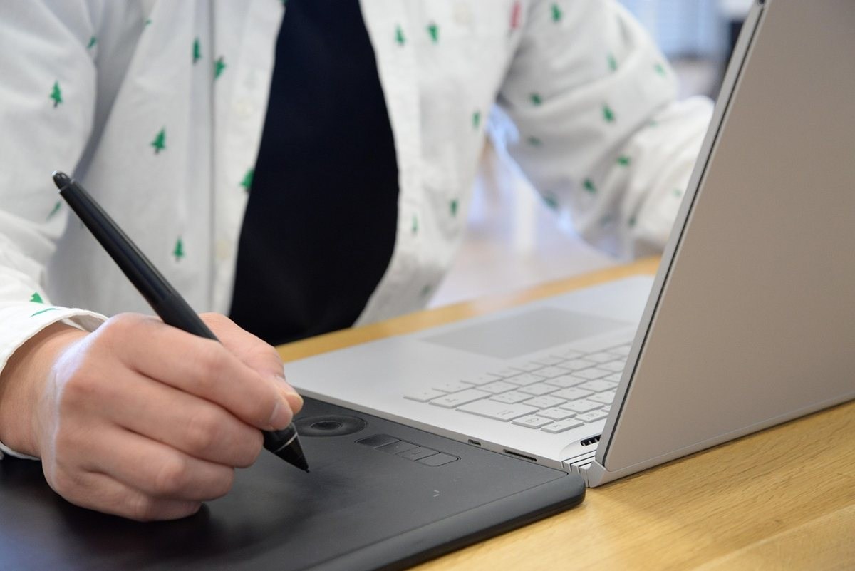 Personne tenant un stylet et dessinant sur une tablette graphique portable en position assise Personne tenant un stylet et dessinant sur une tablette graphique portable en position assise