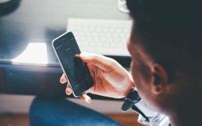 Un homme tient un smartphone noir, regarde l'écran, clavier à l'arrière-plan