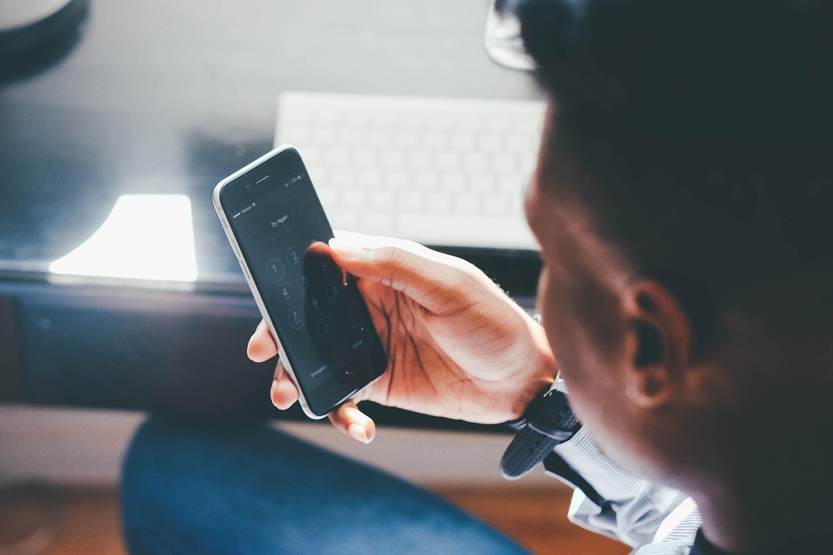 Un homme tient un smartphone noir, regarde l'écran, clavier à l'arrière-plan