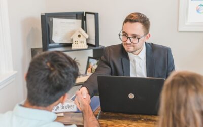 Homme en costume saluant un autre individu devant un ordinateur portable dans un bureau