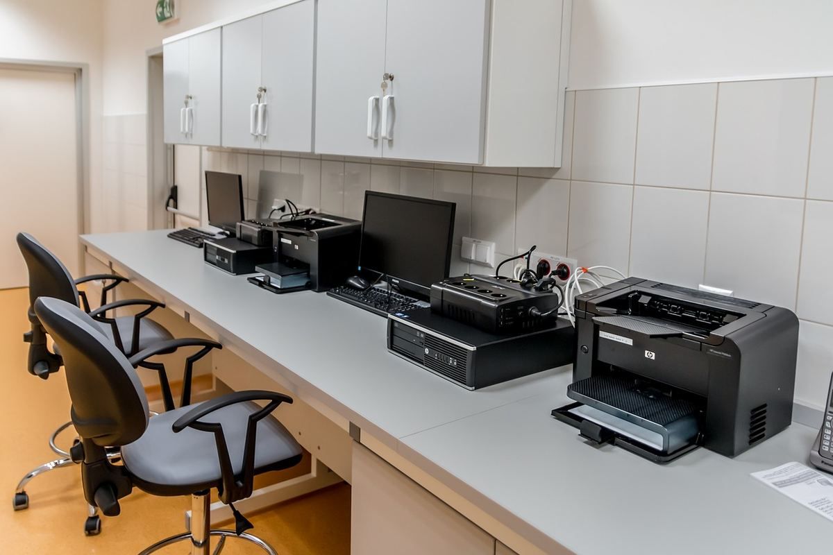 Salle de travail équipée d'ordinateurs et d'imprimantes avec chaises devant les bureaux Salle de travail équipée d'ordinateurs et d'imprimantes avec chaises devant les bureaux