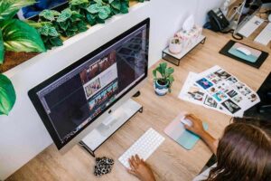 Femme travaillant sur un ordinateur avec feuilles photos et plantes à proximité