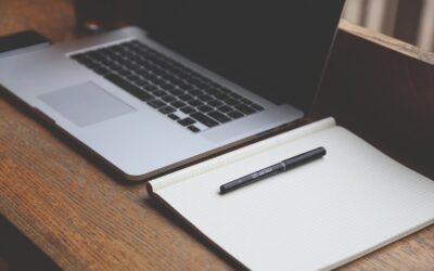 Un ordinateur portable ouvert à côté d'un cahier avec un stylo