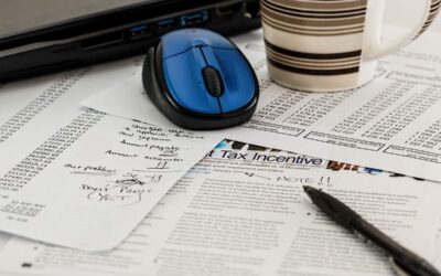 Des papiers fiscaux, une souris bleue, une tasse et un stylo sur un bureau